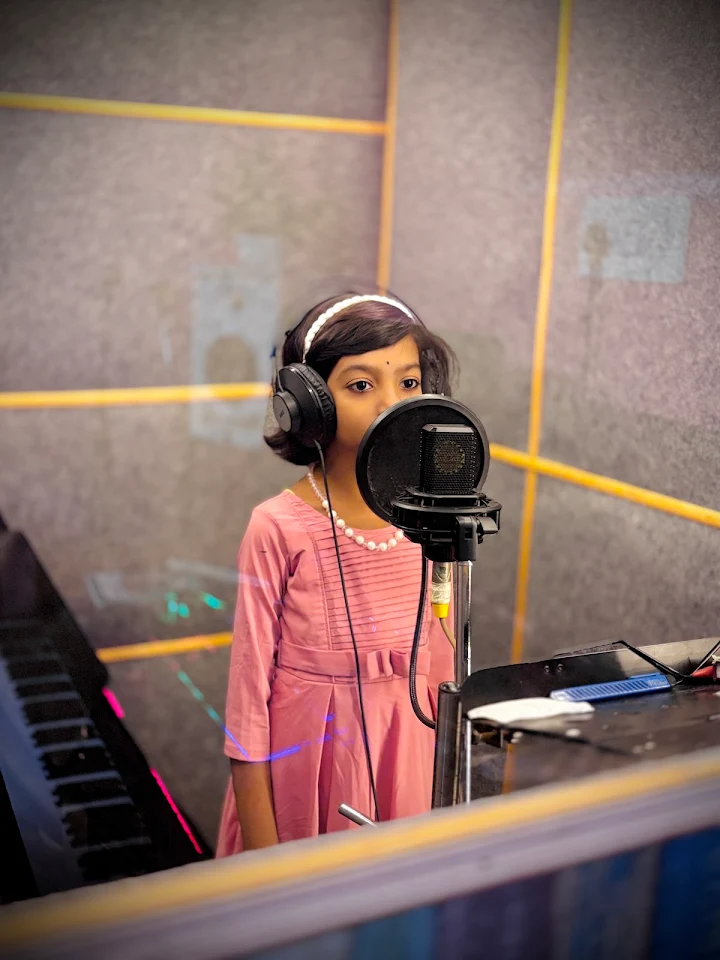 Young singer at the microphone, with a keyboard beside her in the booth