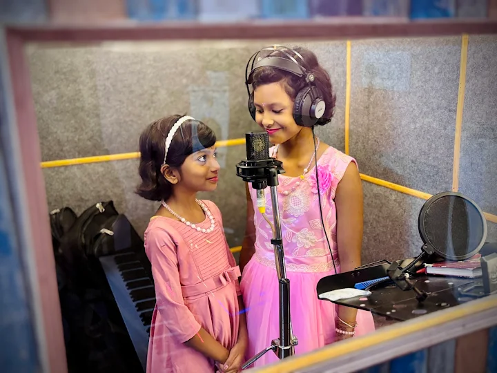 Two young singers sharing a microphone in the vocal booth
