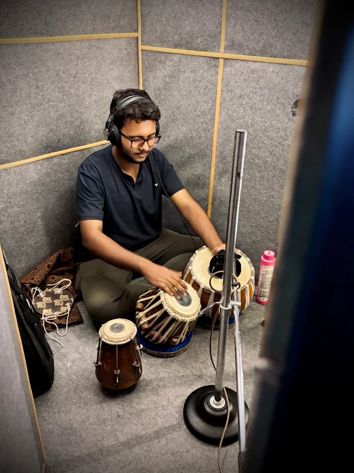 Tabla player recording in the vocal booth, wearing studio headphones